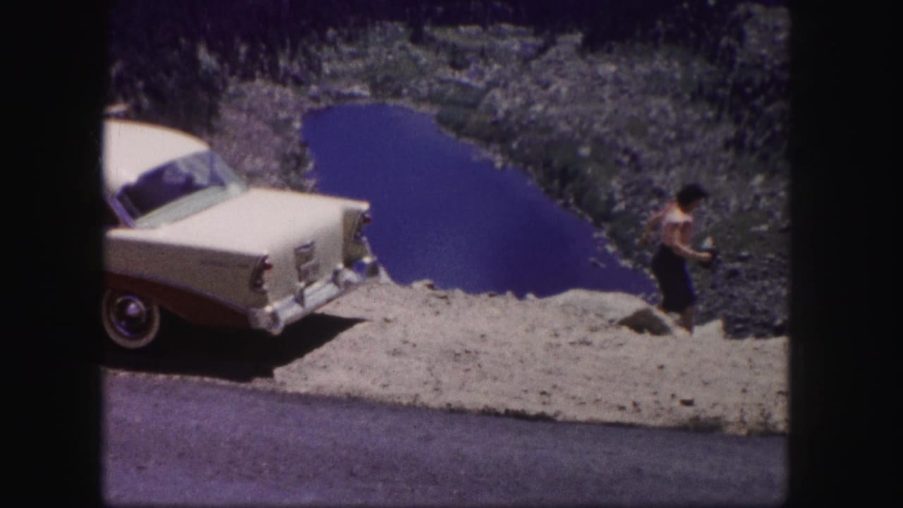 1958 Colorado 8mm frame showing a classic car at a gravel turnout above a mountain lake, with a small figure near the edge.