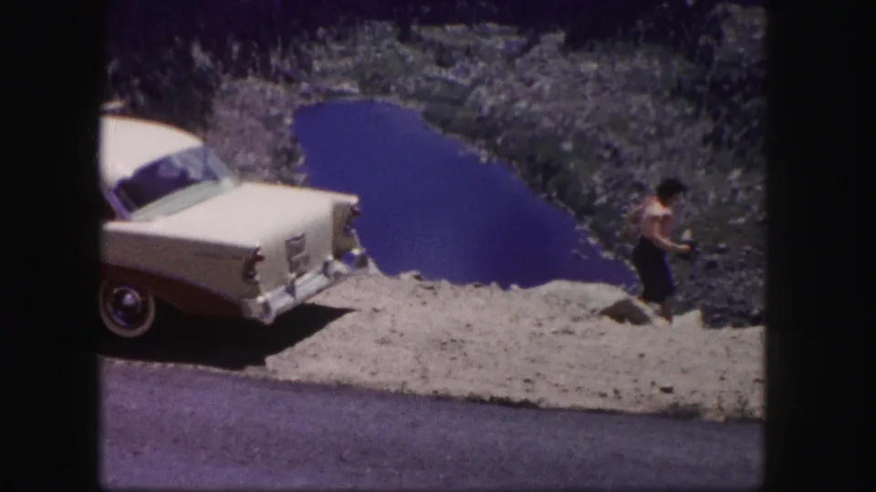 1958 Colorado 8mm frame showing a classic car at a gravel turnout above a mountain lake, with a small figure near the edge.