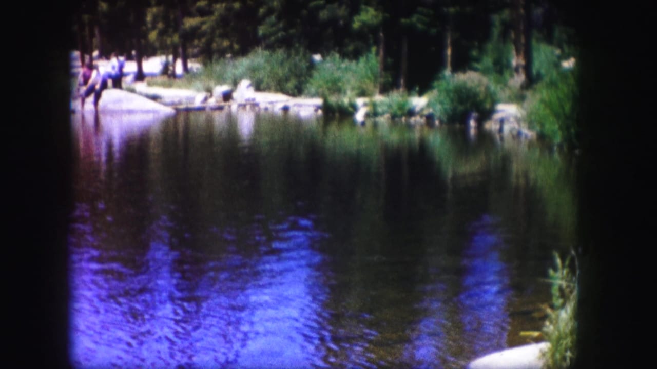 Calm lake with tree reflections and people on a rocky shore.