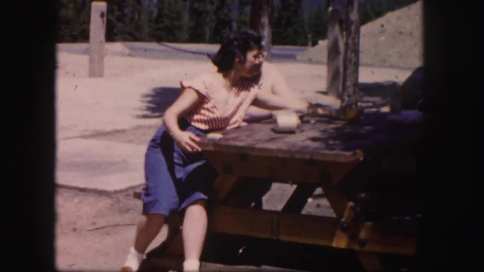 The final frame shows the striped-top woman seated at the picnic table while her companion remains partly visible behind her.