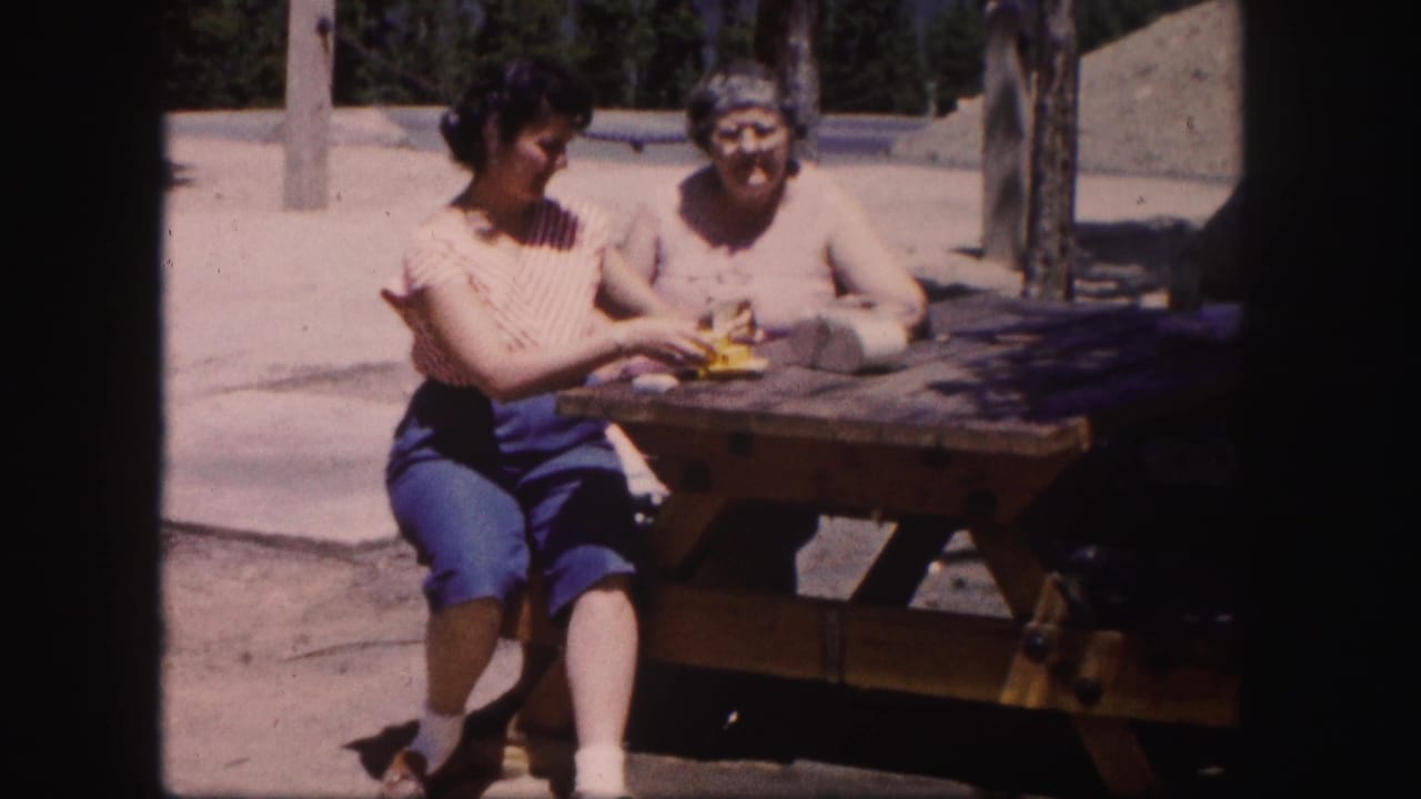 Two women sit at a picnic table, one handling a small yellow object.