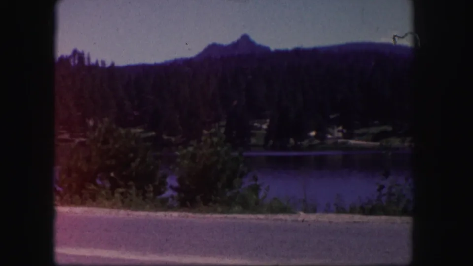 A soft 8mm view shows a lake, roadside edge, trees, and a distant mountain ridge in Colorado.