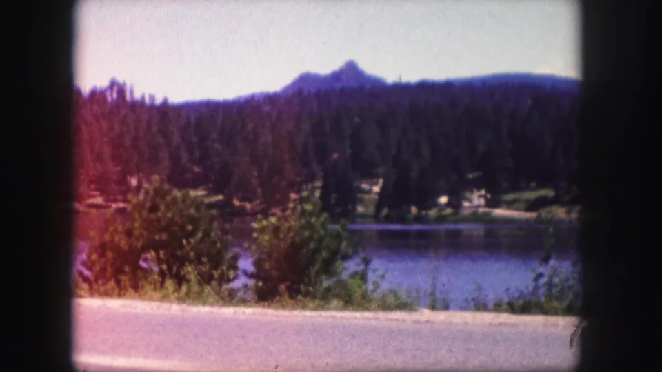 1958 Colorado 8mm frame showing lake water, forested hills, a distant mountain peak, and a warm red color shift along the left side.