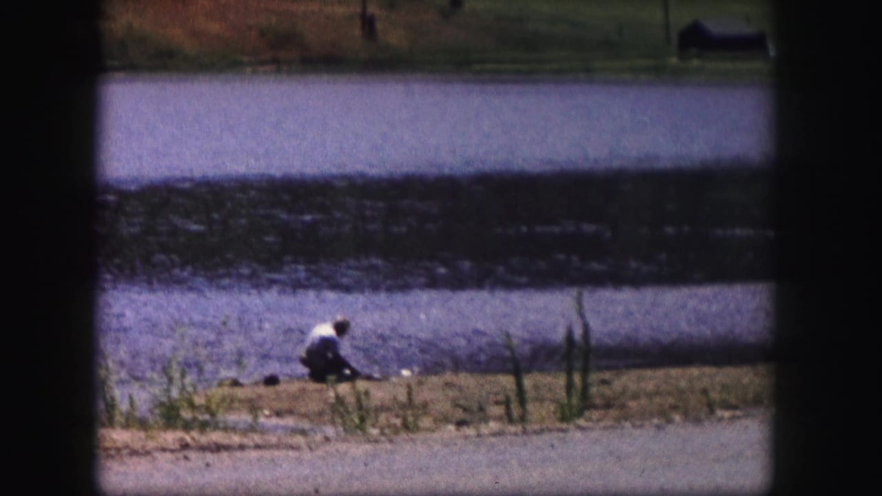 A distant person in light clothing crouches at the edge of a Colorado lake in this 1958 home-movie frame.