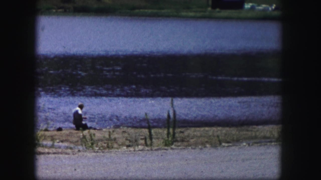 A lone adult fisherman sits at the edge of a Colorado lake in this 1958 home-movie frame.