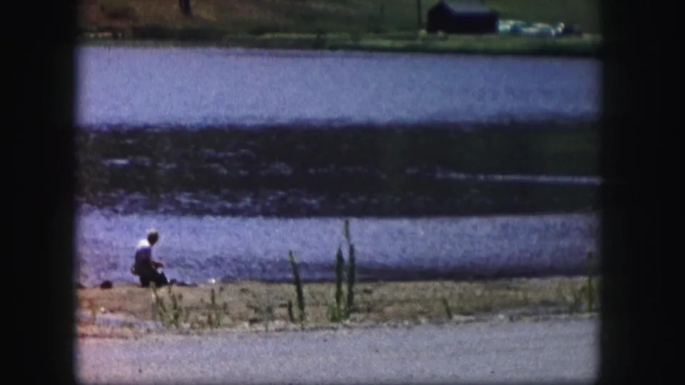 Vintage 8mm view of a man fishing from a sandy lakeside edge in Colorado, 1958.