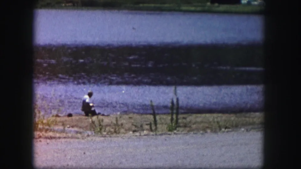 A 1958 Colorado 8mm frame shows the fisherman still seated near reeds along the lake edge.