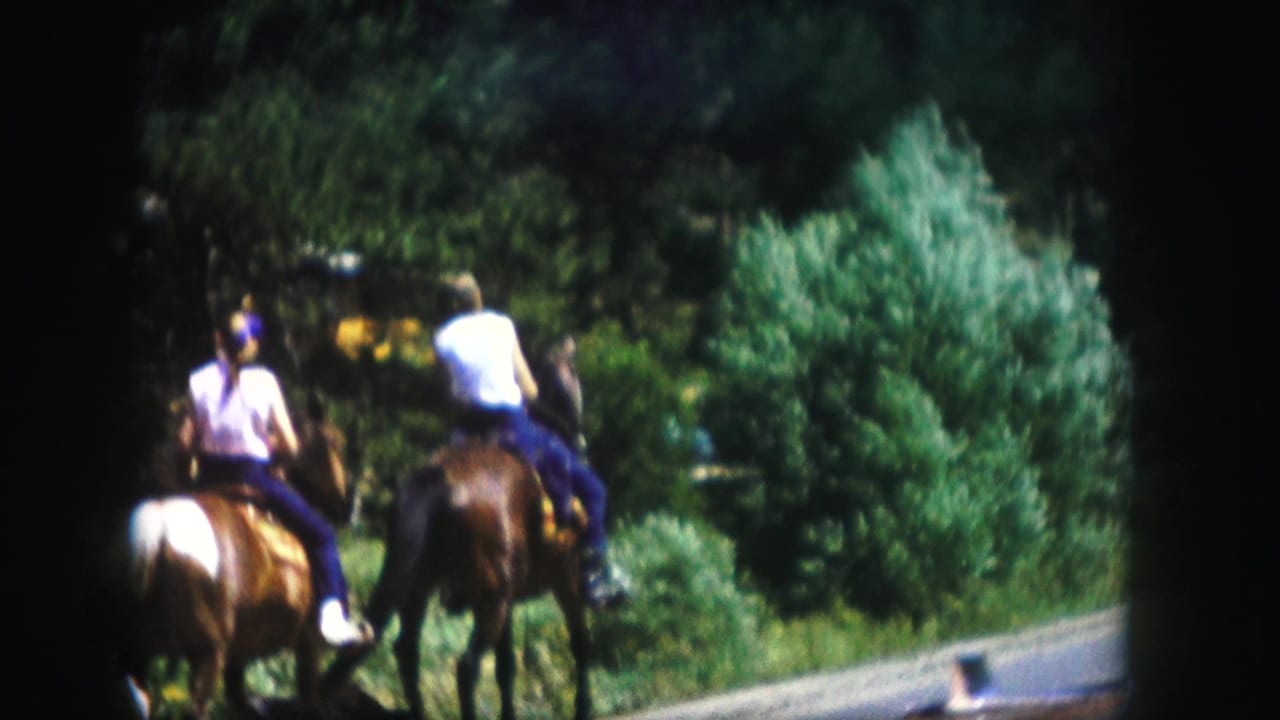Two men ride horses away from the camera on a forest road in Colorado, supported by the 1958 home-movie metadata.