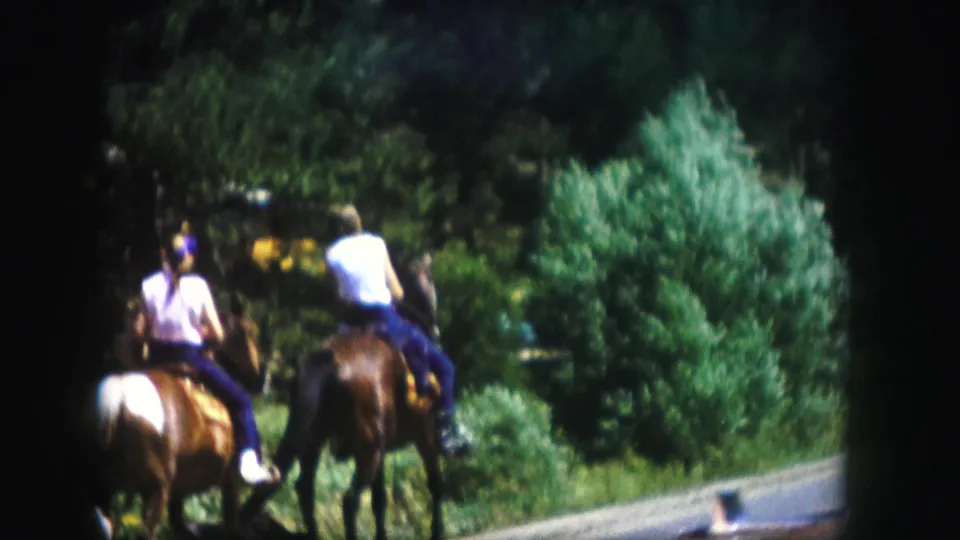 Two men ride horses away from the camera on a forest road in Colorado, supported by the 1958 home-movie metadata.