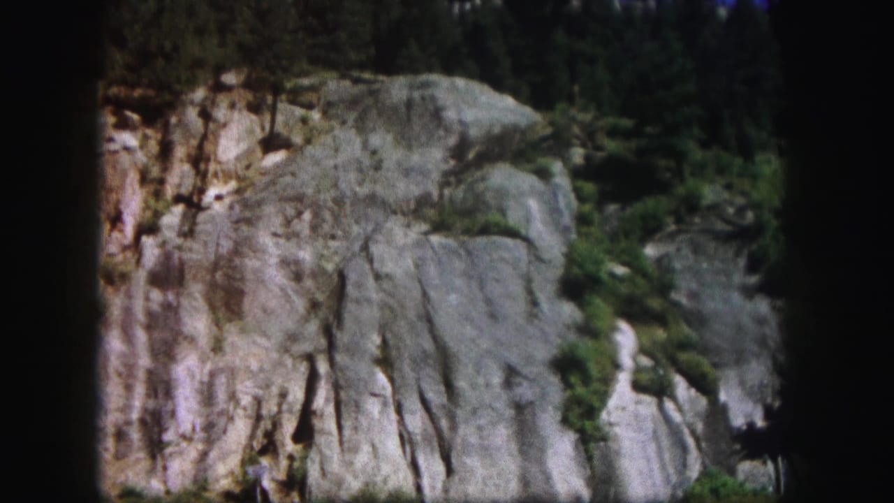 1958 Colorado 8mm frame showing a steep rock face with vertical fissures, sparse greenery, and dark gate edges.