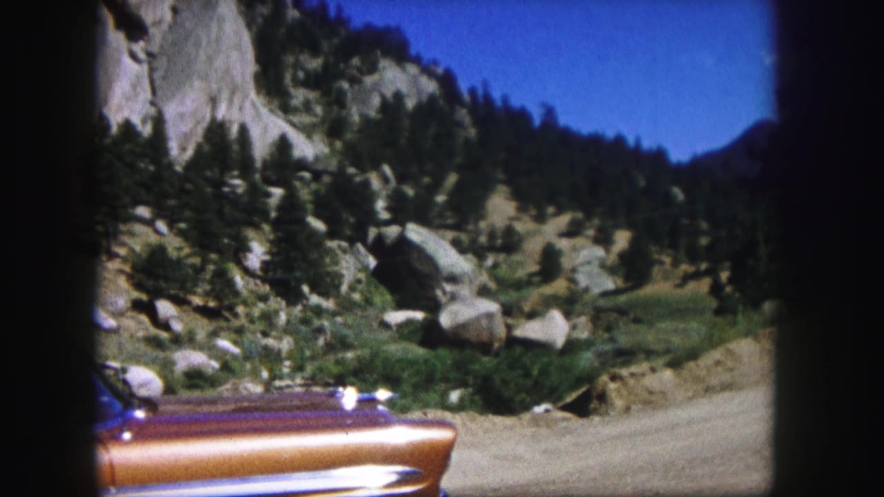 Parked vintage car partly visible at the edge of a rocky mountain landscape.