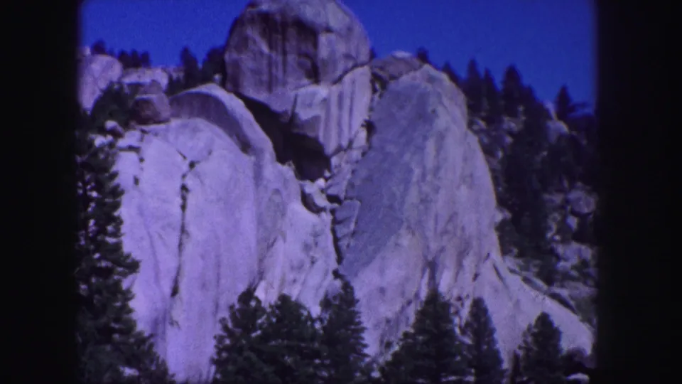 Vintage 1958 Colorado 8mm view of rounded granite outcrops, forested slopes, and purplish film color.