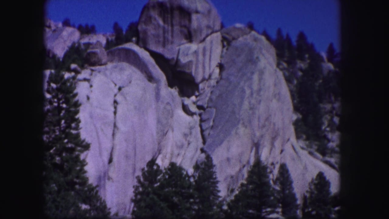 Colorado mountain landscape on 8mm film, with pale rock faces, conifers, blue sky, and visible contact-sheet frame edges.