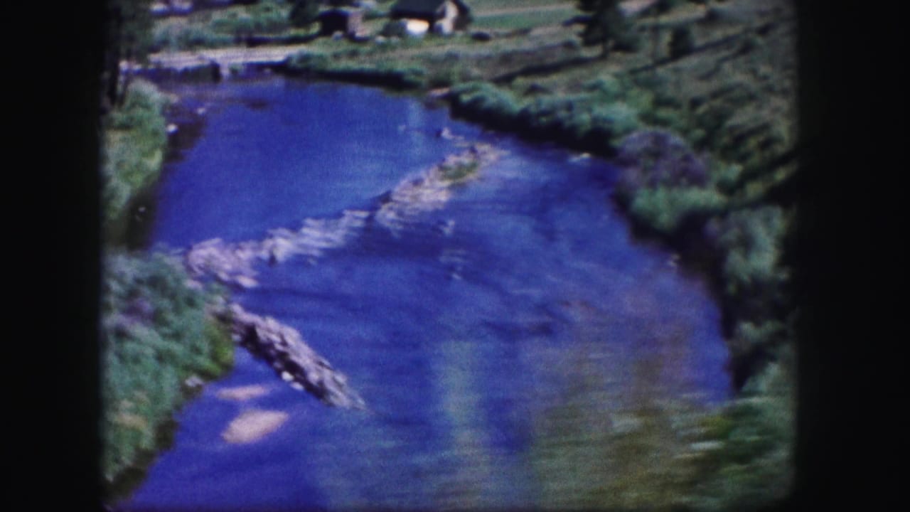 River channel with rocks, green banks, and a dark vertical film edge.
