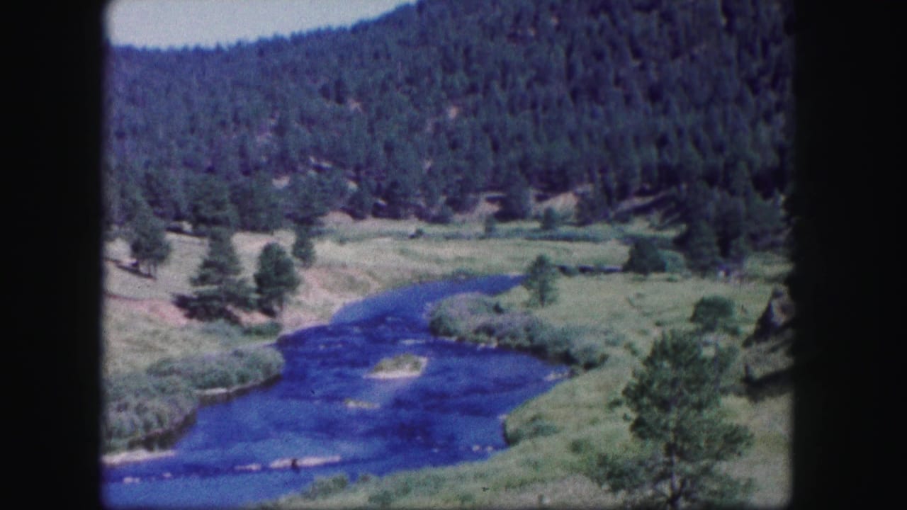 1958 Colorado 8mm frame showing a winding river, open valley, and pine-covered hills from an elevated viewpoint.