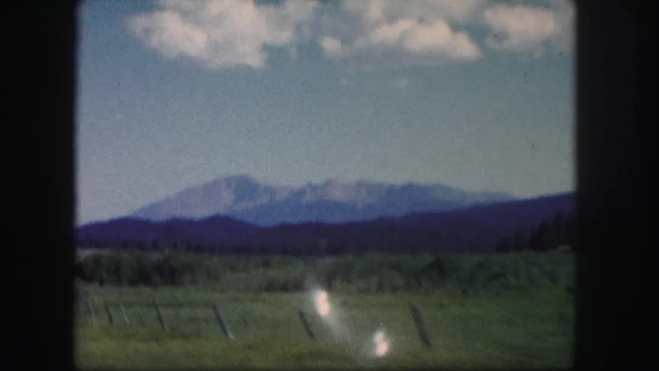 1958 Colorado 8mm frame showing distant mountains, grassy foreground, possible fence posts, and soft home-movie color.