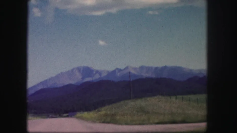 Colorado mountain landscape from a 1958 home movie, with grassland, a utility pole, dark foothills, and pale mountains in the distance.