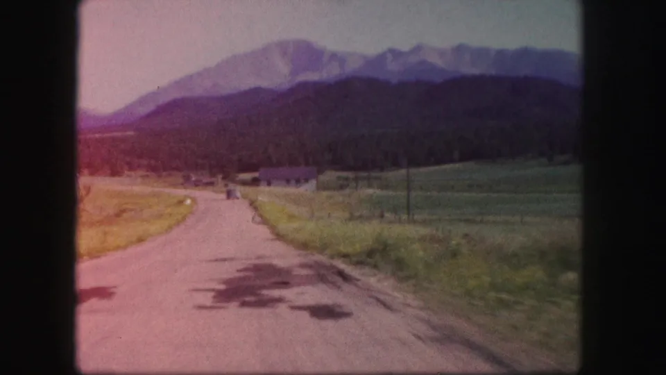 1958 Colorado 8mm frame showing a sunlit rural road, grassy shoulders, distant trees, and mountain peaks with warm color shift.