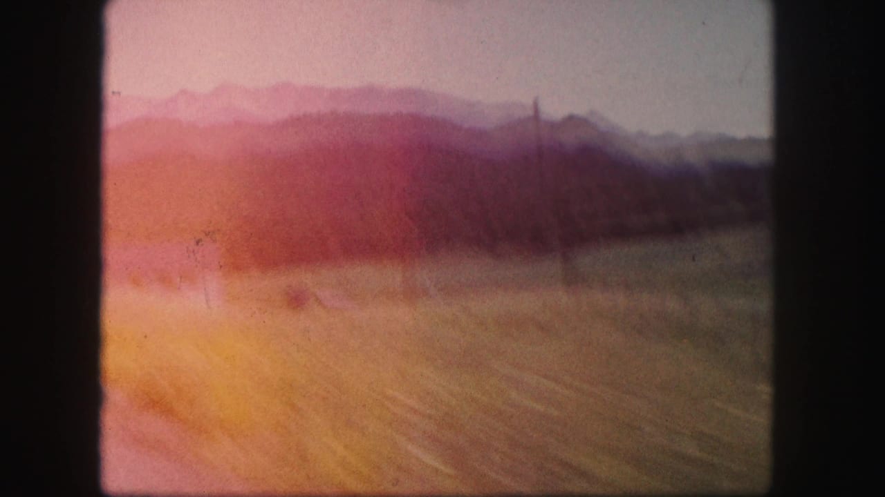 1958 Colorado 8mm frame with a blurred roadside field, distant mountains, and strong pink-orange color shift from the film scan.