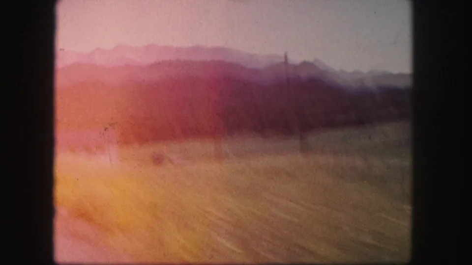 1958 Colorado 8mm frame with a blurred roadside field, distant mountains, and strong pink-orange color shift from the film scan.