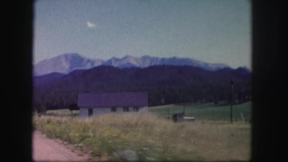 1958 Colorado 8mm frame showing a small rural house near the road, with open grassland and mountains in the background.