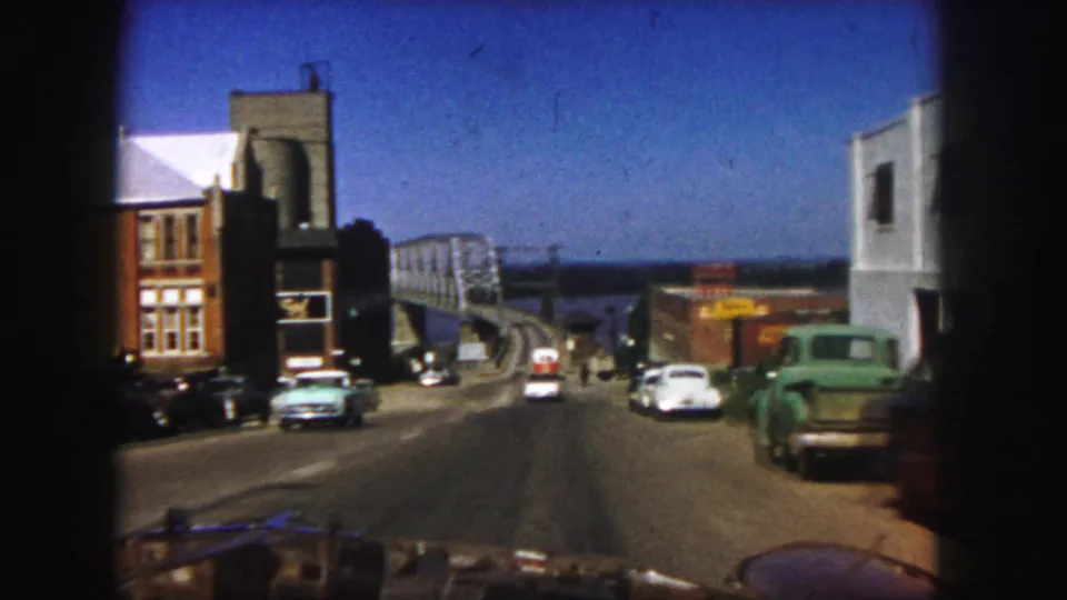 End frame of a 1958 Denver street approach, with period cars, signage, and a bridge near the waterfront.
