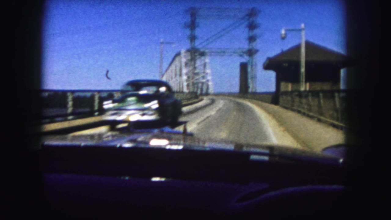 Car view crossing a steel truss bridge with an oncoming automobile.