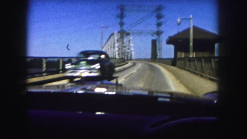 1958 Denver home-movie view from a car driving across a steel truss bridge as another automobile approaches.