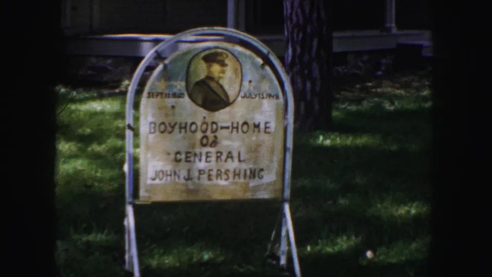 A closer 1958 Denver frame shows the weathered sign reading Boyhood-Home of General John J. Pershing on a shaded lawn.