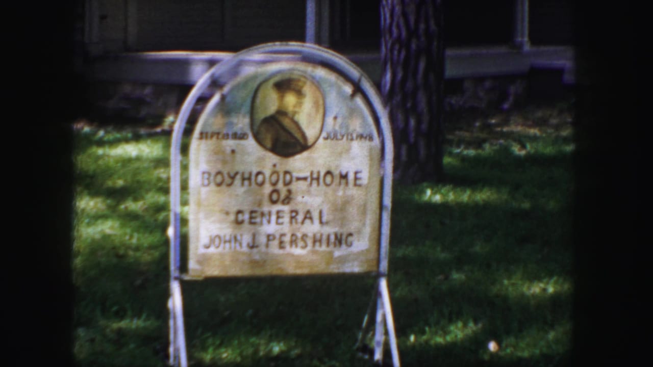 1958 Denver home-movie frame showing an arched Boyhood Home of General John J. Pershing sign with a portrait medallion on grass.