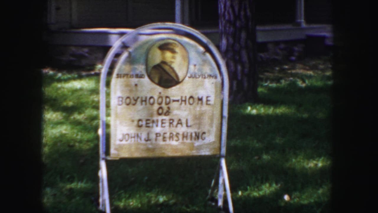 1958 Denver frame of the General John J. Pershing boyhood home sign, with handwritten text, portrait, lawn, and tree shadow.