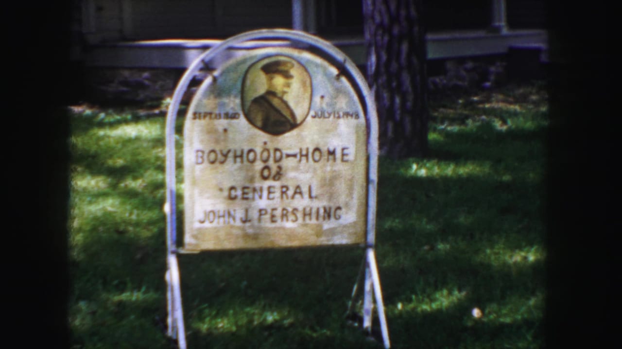 Weathered sign for the Boyhood Home of General John J. Pershing in a grassy yard.