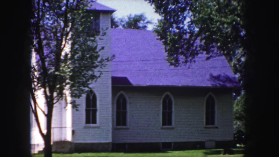 1958 Denver-area frame of the same church exterior, with leafy trees, Gothic-style windows, purple roof, green lawn, and heavy 8mm edge shadow.