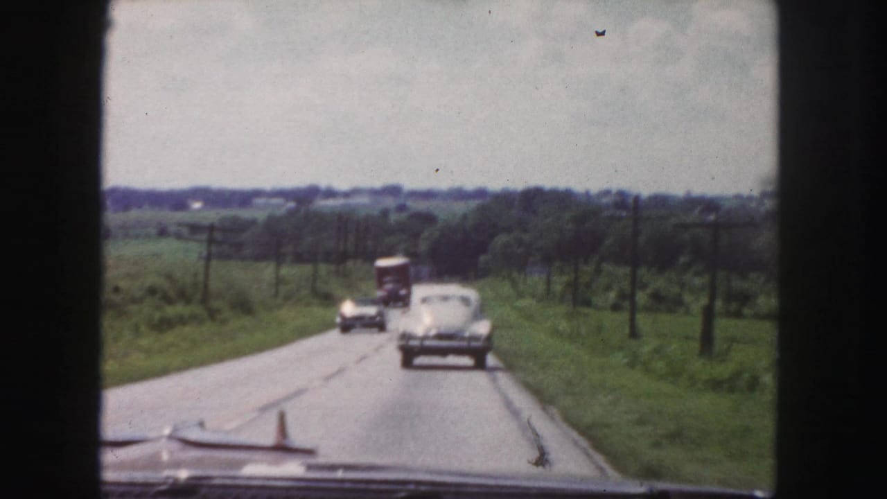 1958 road-view frame near Denver showing classic cars and a truck ahead on a two-lane rural highway with fields and utility poles.