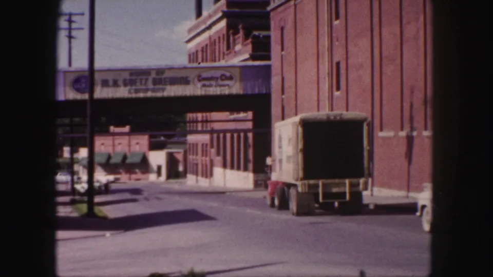A box truck recedes along a Denver brewery-area street, with brick industrial architecture and painted commercial signage visible.