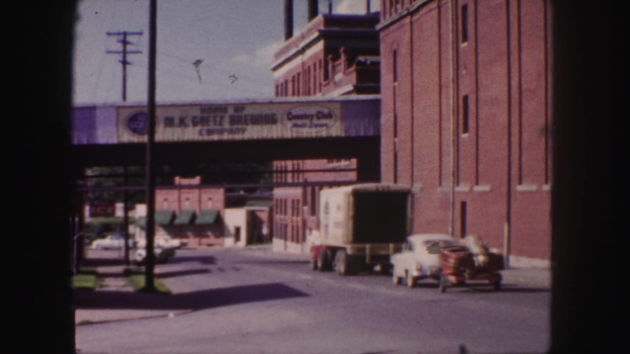 1958 Denver industrial street with truck, white car, parked vehicles, and visible Goetz Brewing advertising over the roadway.