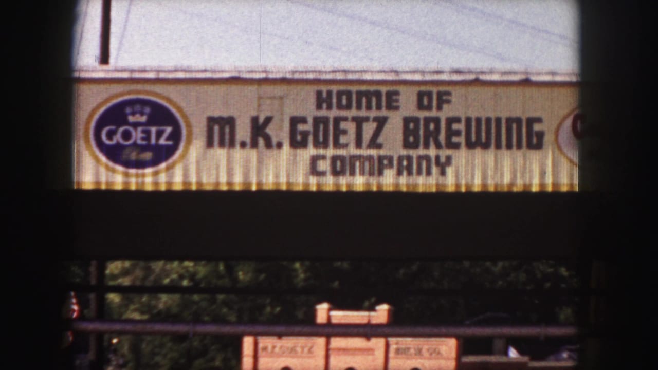 M.K. Goetz Brewing Company sign with Goetz logo above a shaded street area.