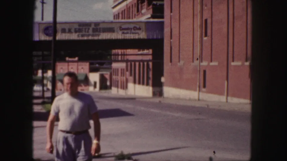 1958 Denver 8mm frame with an adult man in the foreground and the M.K. Goetz Brewing Company exterior behind him.
