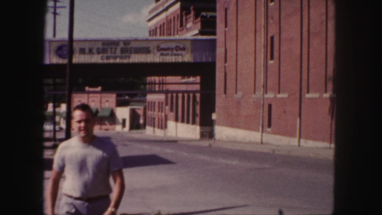 1958 Denver street view with a man walking past brick buildings and the M.K. Goetz Brewing Company bridge.
