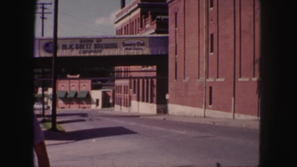 1958 Denver view of the M.K. Goetz Brewing Company bridge with brick buildings and a cropped passerby.
