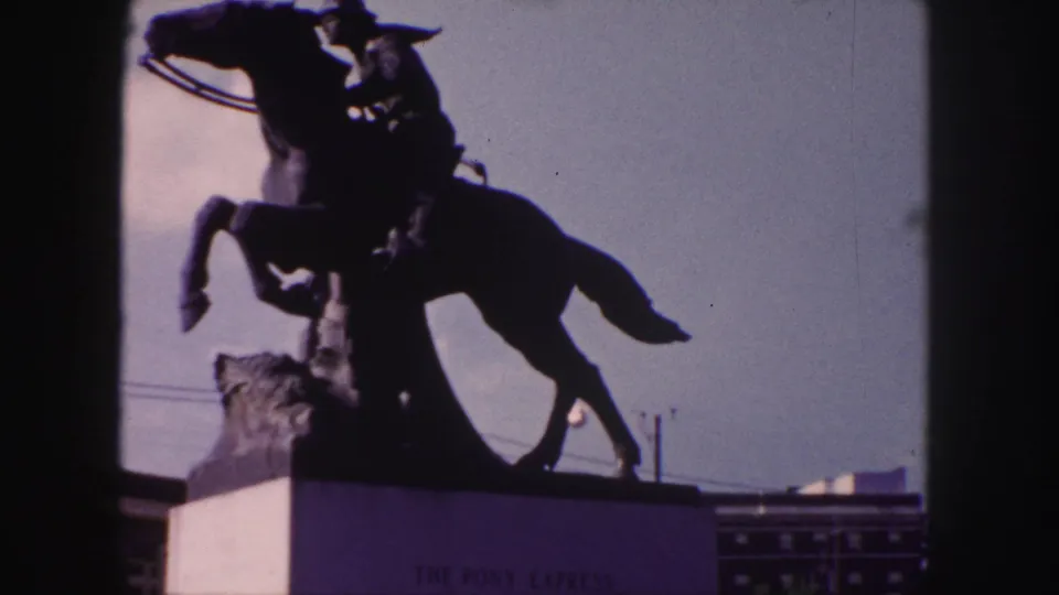 1958 Denver home-movie frame showing the Pony Express equestrian statue in silhouette, partly bordered by dark frame edges.