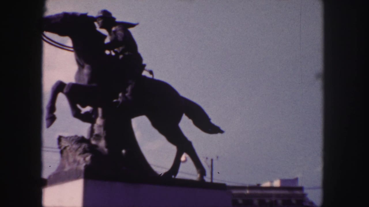1958 Denver home-movie frame showing a dark equestrian statue and rider silhouetted against the sky.