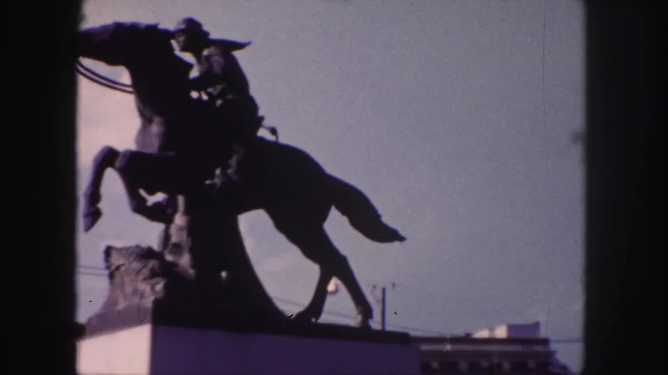 1958 Denver home-movie frame showing a dark equestrian statue and rider silhouetted against the sky.