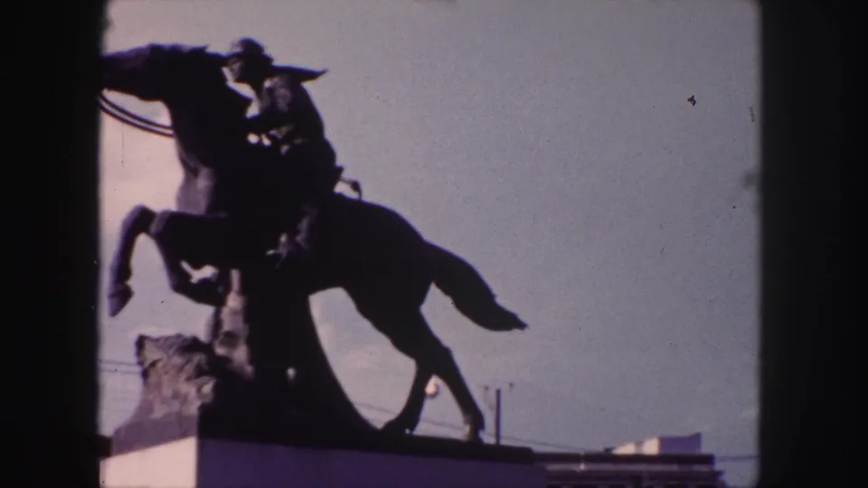 Denver 1958 frame of the horse-and-rider monument, seen in silhouette with roofline and sky behind it.