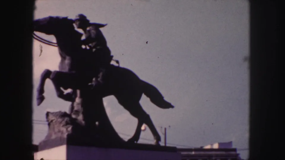 A 1958 Denver home-movie view shows the equestrian statue still silhouetted, with the roof edge and sky visible.