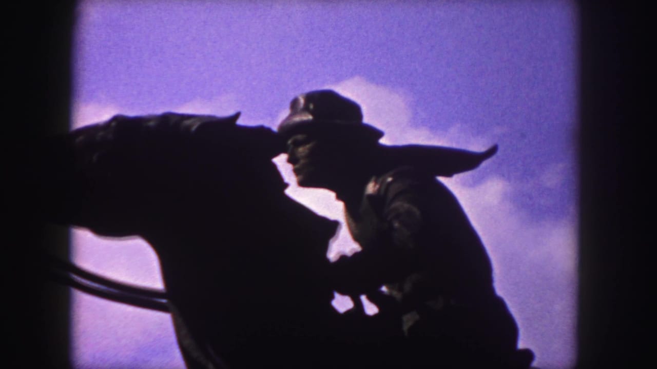 1958 Denver 8mm frame showing a dark mounted cowboy statue in profile against a purple-blue sky and clouds.
