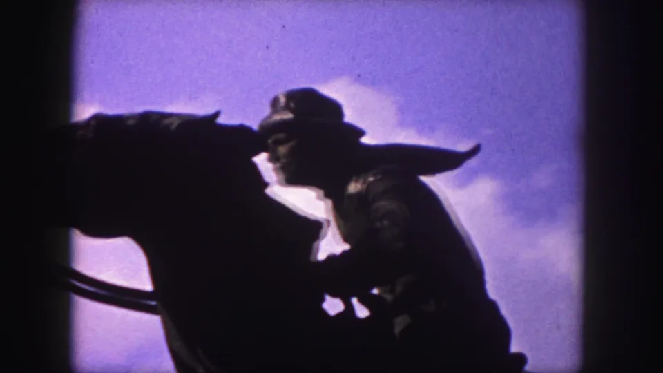 Denver home-movie frame from 1958 showing the statue's rider, horse head, and reins as a dark silhouette against clouds.