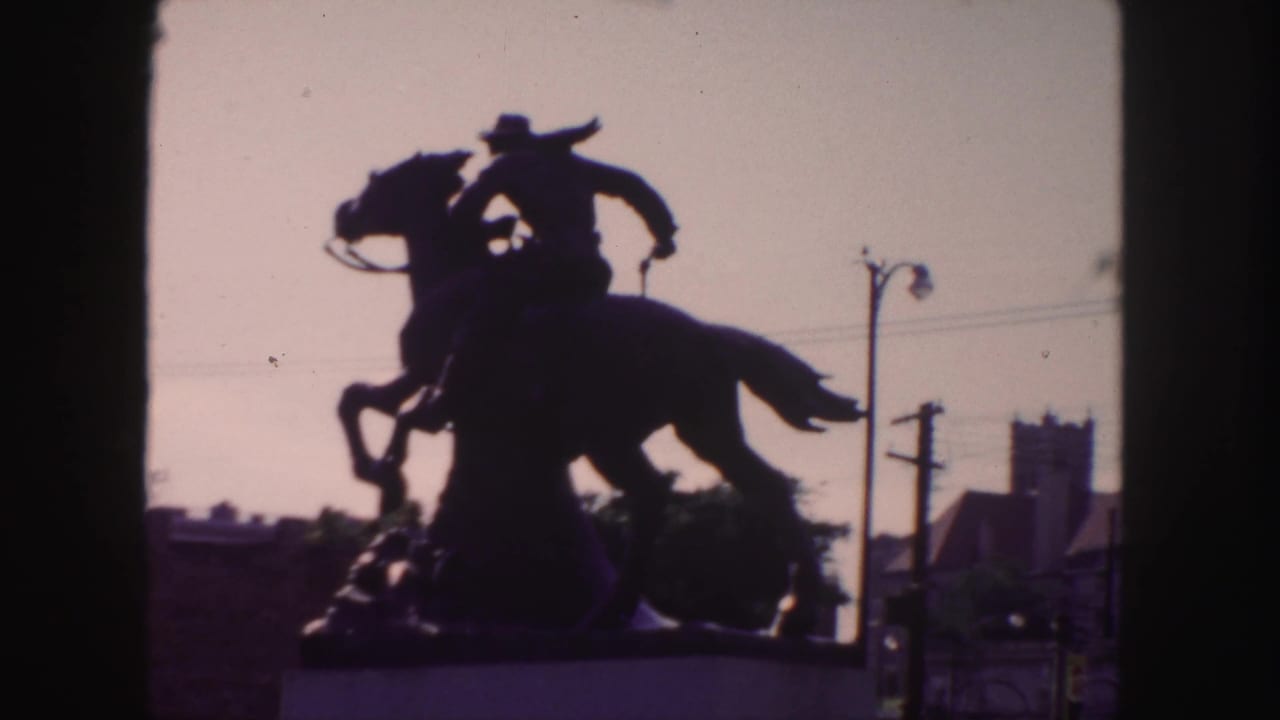 Backlit equestrian statue with horse and rider silhouetted beside streetlights and utility poles.