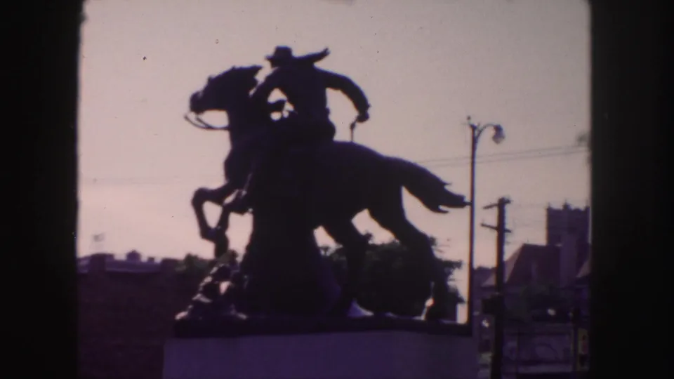 1958 Denver 8mm frame showing the equestrian statue as a silhouette, with pedestal and mid-century street infrastructure visible.