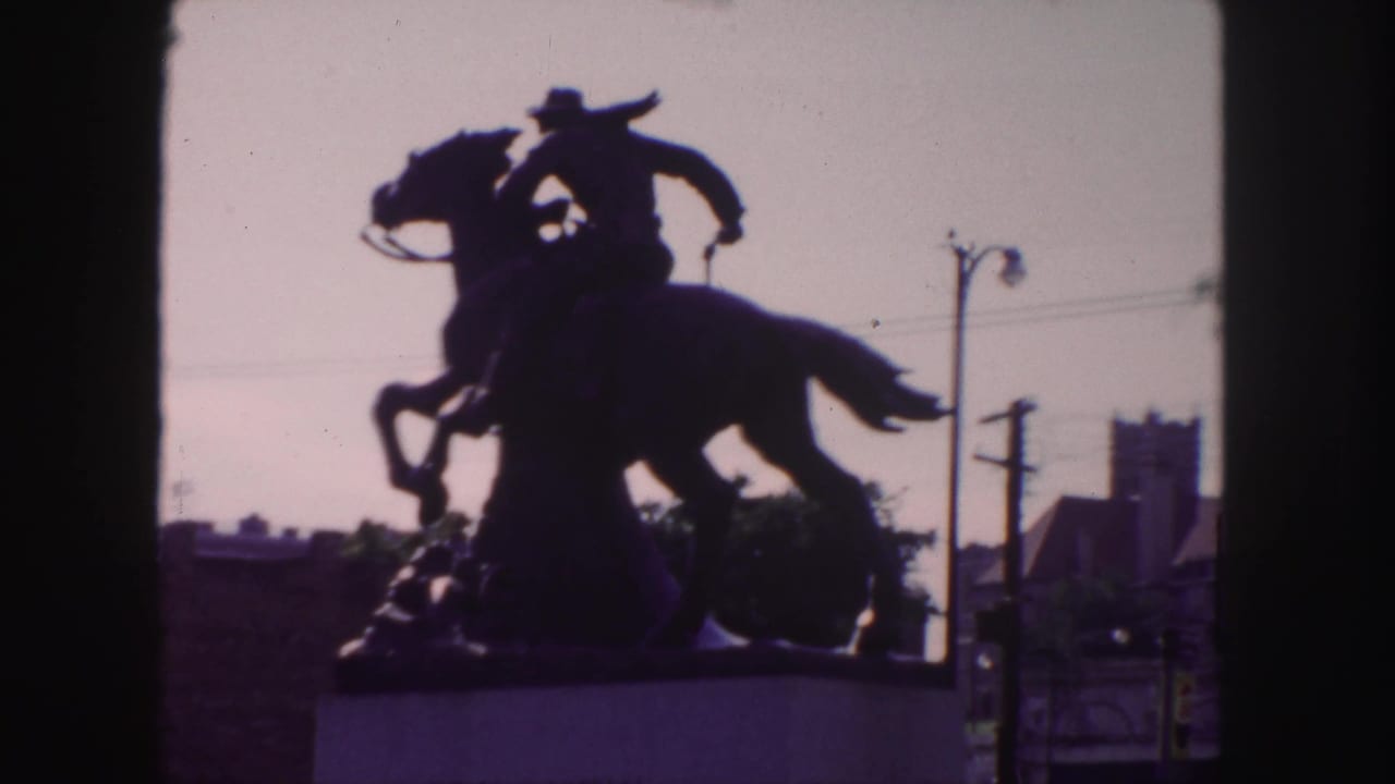 Silhouetted cowboy on horseback statue against a dim sky with utility poles nearby.